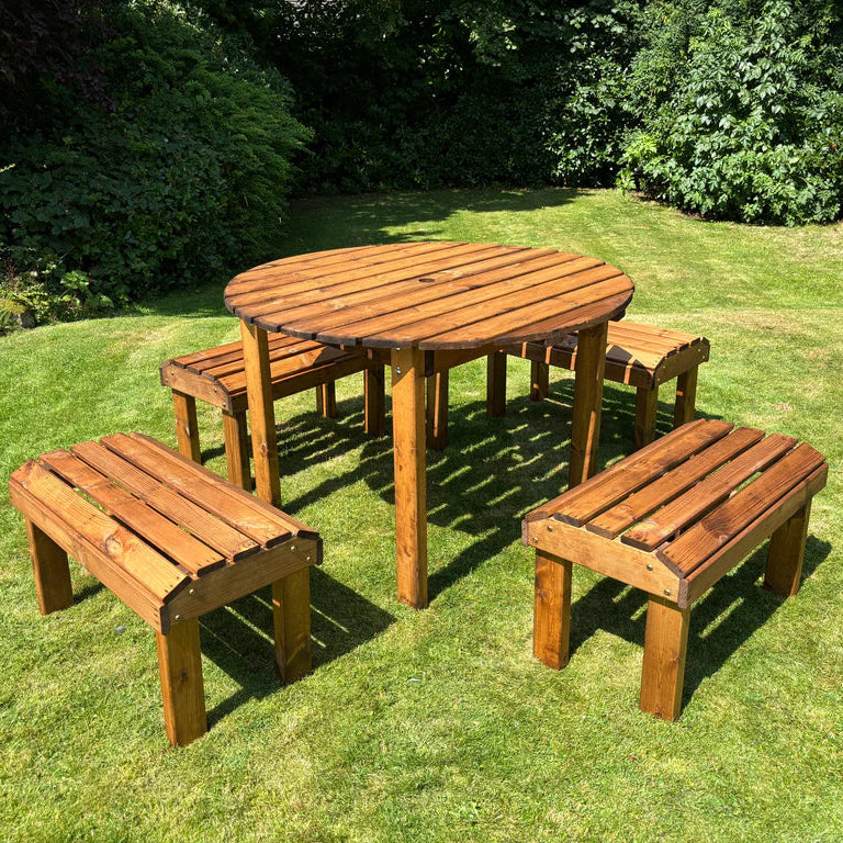 KNIGHTS FOUR SEATER ROUND TABLE SET - table set on the grass in the sunshine, surrounded by bushes and trees. 