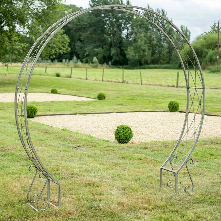 An Ascalon metal moon gate in mottled green stood on a lawn with trees in the background