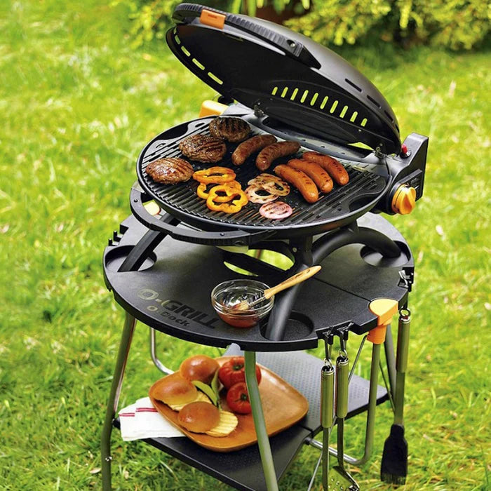 A black o-grill 600 being used to cook sausages and veggies outdoors